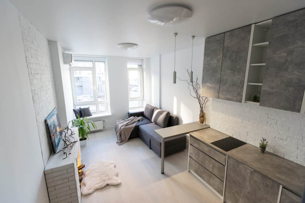 Modern minimalist living room with gray sofa, kitchen, and white brick accent wall