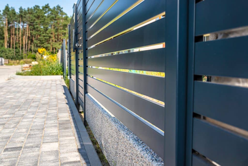 Modern dark metal fence with horizontal slats along paved walkway near residential area