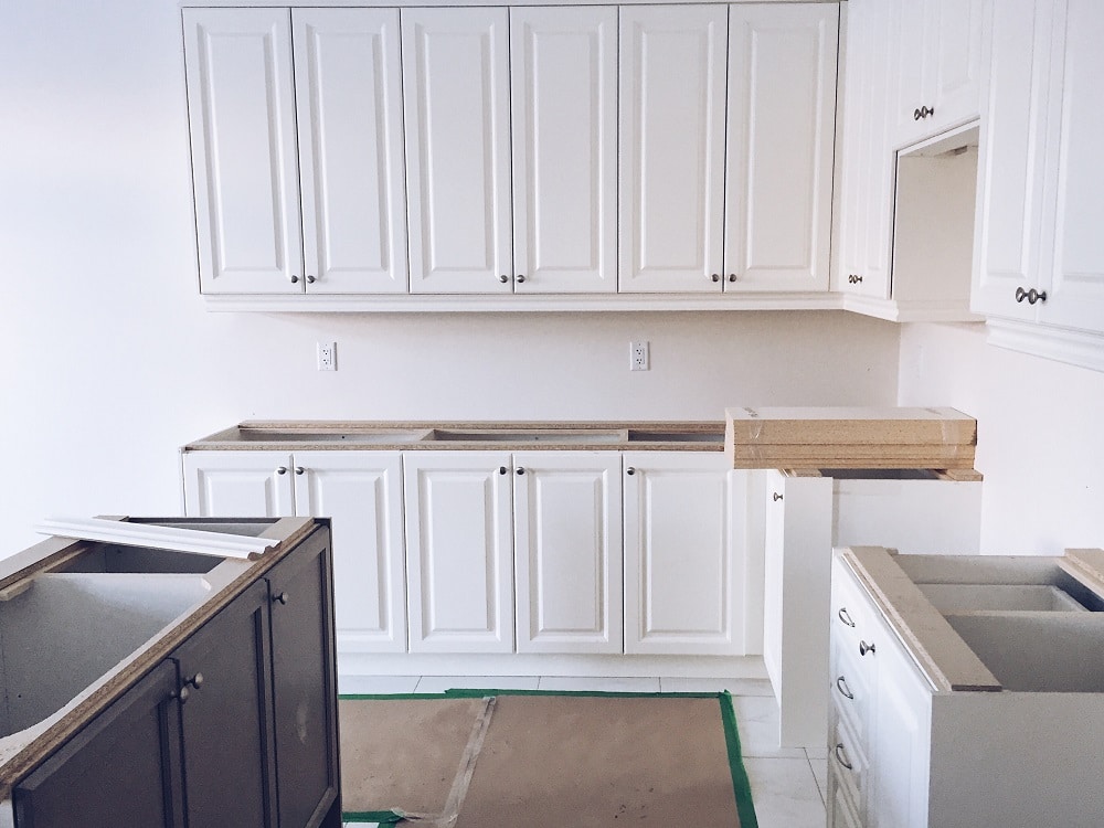 Kitchen renovation in progress showing white cabinets being installed with temporary wood countertops